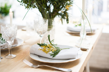 Beautiful springtime table setting with green leaves and mimosa branches, bright white table dinner decoration