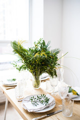 Beautiful springtime table setting with green leaves and mimosa branches, bright white table dinner decoration