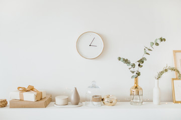 Modern interior design concept. Bright beige and golden apartment with clock, eucalyptus branch, vase, candle.