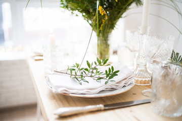 Beautiful springtime table setting with green leaves and mimosa branches, bright white table dinner decoration