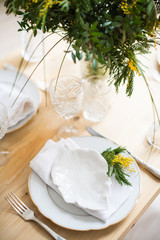 Beautiful springtime table setting with green leaves and mimosa branches, bright white table dinner decoration