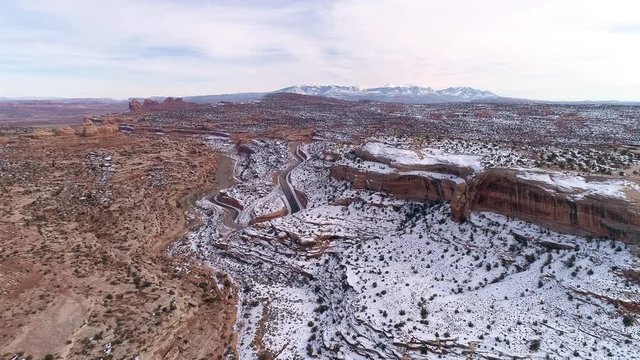 Aerial view flying towards road winding through the desert with snow covering part of the landscape near Moab Utah.