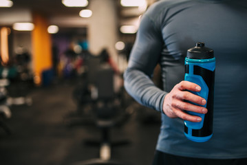 Athletic man holding water bottle in the hand in the gym, close-up.