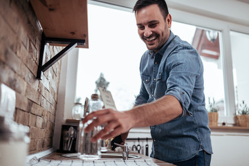 Happy man in denim shirt washing dishes at home, low angle image.