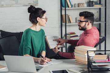 Obraz premium handsome man pointing with finger at book near attractive coworker in modern office
