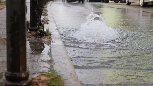 Footage of water comming out from a road drainage due to a ruptured water pipe under the ground, a car passing by...