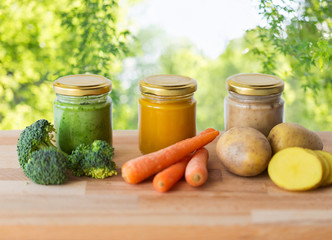 baby food, healthy eating and nutrition concept - vegetable puree in glass jars on wooden table over green natural background