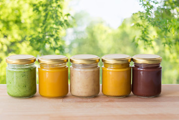 healthy eating, baby food and nutrition concept - vegetable or fruit puree in glass jars on wooden table over green natural background