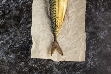 Smoked mackerel without head on baking paper on black background