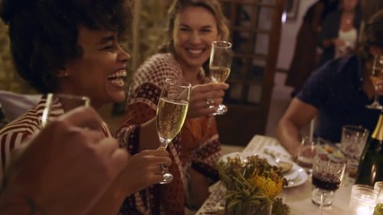 Multi-ethnic friends sitting at dinner table and having drinks at party. Young people at partying together and having drinks.