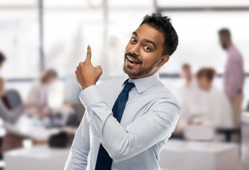 business and people concept - smiling indian businessman in shirt with tie pointing finger at something invisible over office background