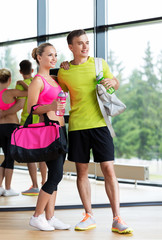 sport, fitness, lifestyle and people concept - smiling couple with water bottles and bags in gym