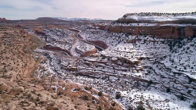 Aerial view flying through desert canyon and over winding road in the snow as it cuts into the landscape near Moab Utah.