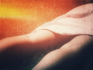 Sunburn concept. Legs and skirt of a woman sunbathing on grass. Distressed image. Mobile phone photo with some phone or tablet post processing.