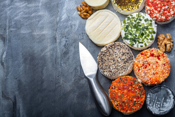 Assortment of French fresh white soft goat cheeses with different tastes topping made with herbs, paprika, indian curry, bruscetta, chives and dried tomatoes