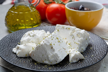 Fresh young soft white Feta cheese on black plate seasoned with dried oregano herb