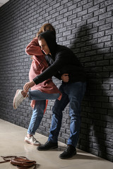 Young woman defending herself from attack by thief near dark brick wall