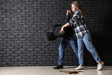Young woman defending herself from attack by thief near dark brick wall