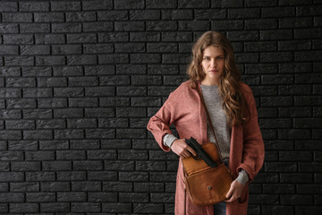 Young woman with gun for self-defence against dark brick wall