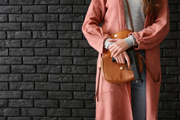 Young woman with gun for self-defence against dark brick wall