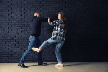 Young woman defending herself from attack by thief near dark brick wall