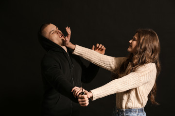 Young woman defending herself from attack by thief on dark background