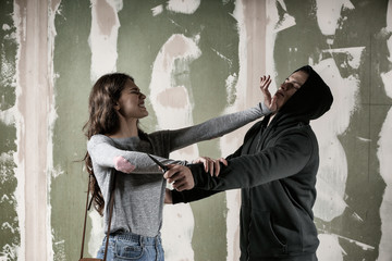 Young woman defending herself from attack by thief on color background