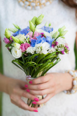 Closeup view of cute small colorful bridal wedding bouquet of flowers in hands of young beautiful bride. Vertical color photography.