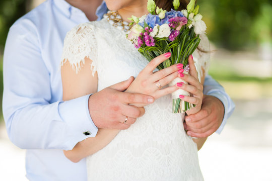 Bride and groom portrait. Beautiful pink bridal manicure. Bride holding cute small bouquet of flowers in hands. Horizontal color photography.