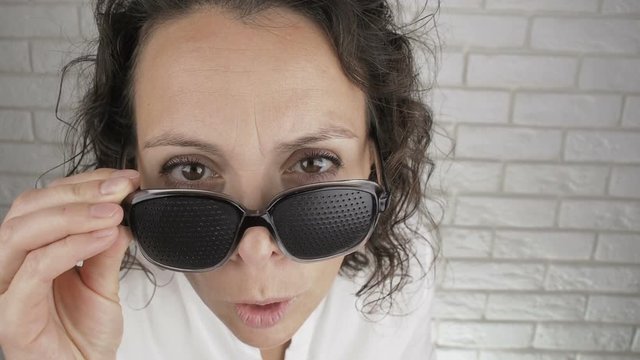 Woman wearing pinhole glasses looking into camera. Surprised woman takes off her pinhole glasses.