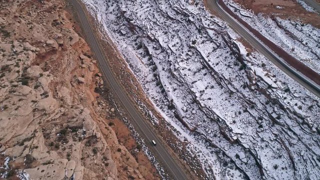 Aerial view of winding road with mail truck driving its route through the vast desert landscape with snow in Moab Utah.