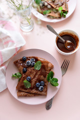 Homemade chocolate crepes served with blueberries, sauce and mint leaves on pink background. Selective focus. Top view. Copy space