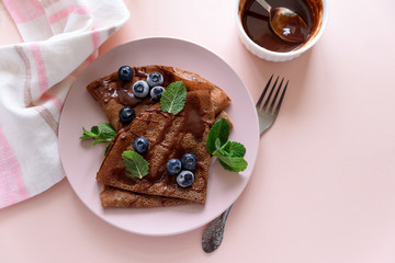 Homemade chocolate crepes served with blueberries, sauce and mint leaves on pink background. Selective focus. Top view. Copy space