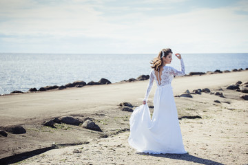 Fashionable bride in elegant wedding dress walking on the coast of ocean. Beauty, emotional, lifestyle concept
