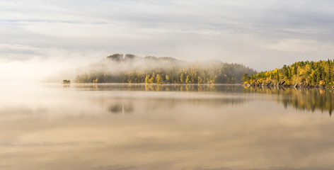 Foggy autumnal morning by the lake. Natural sunrise light. Trondheim area in Norway.