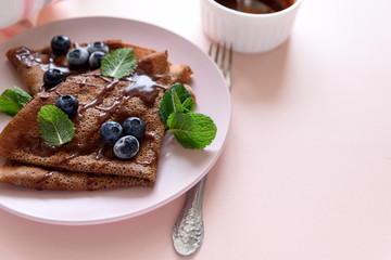 Homemade chocolate crepes served with blueberries, sauce and mint leaves on pink background....