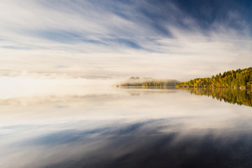 Foggy autumnal morning by the lake. Natural sunrise light. Trondheim area in Norway.
