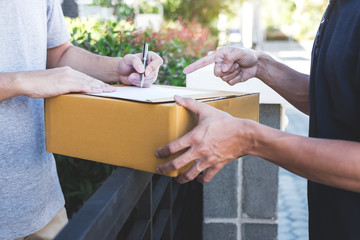 Obraz premium Delivery mail man giving parcel box to recipient, Young man signing receipt of delivery package from post shipment courier at home