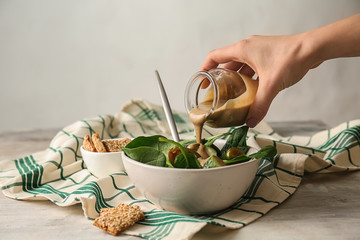 Pouring of tasty tahini from jar onto fresh vegetables in bowl