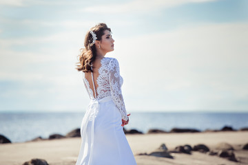 Fototapeta na wymiar Fashionable bride in elegant wedding dress walking on the coast of ocean. Beauty, emotional, lifestyle concept