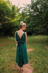 Back view of the young lady in the green dress who is standing in the garden and looking aside