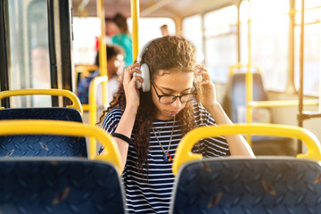 Cute curly girl sitting in a bus and listening to music.