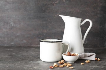 Mug and jug of fresh milk with nuts on grey table
