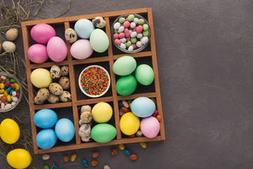 Fototapeta na wymiar Colored easter eggs and small candies in frame on gray background