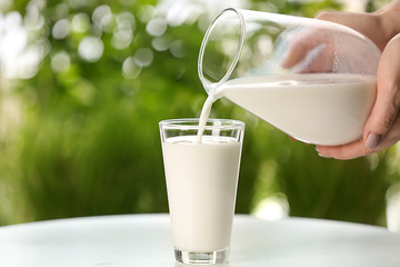 Woman pouring fresh milk from jug into glass on table