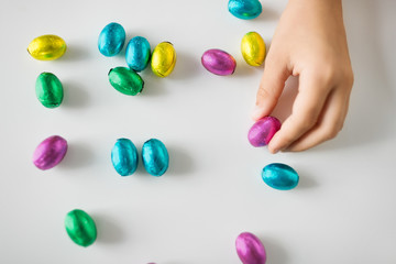 easter, holidays and people concept - hand of child with chocolate eggs or candies in foil wrappers
