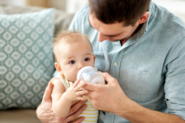 family, fatherhood and people concept - father helping little baby daughter with drinking from...