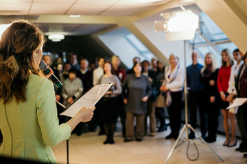 The girl is reading into the microphone in front of the audience.