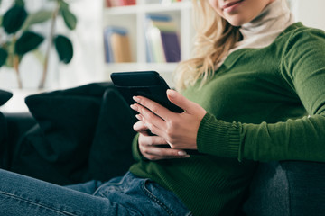 cropped view of woman studying with ebook while sitting on sofa