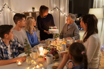dinner party and celebration concept - happy family with cake celebrating grandfathers birthday at...